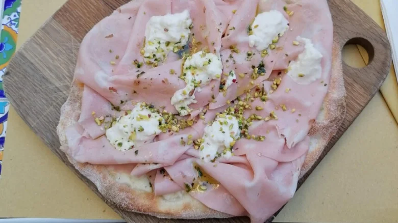 Hotová pinsa s uzeným masem a sýrem na dřevěném prknu.