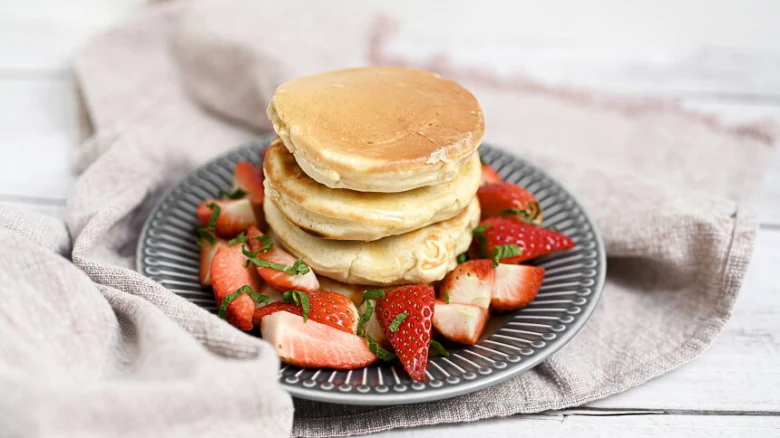 Skládané lívance s jahodami na šedém talíři.