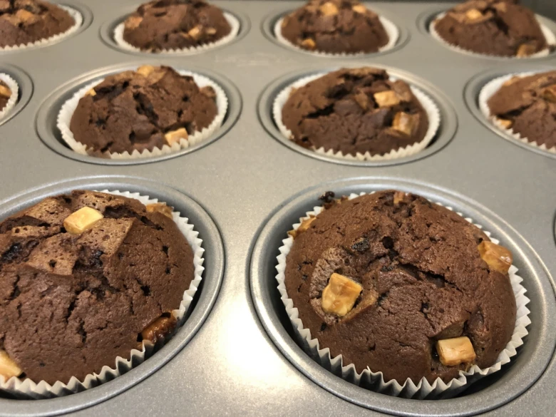 Čokoládové muffiny s kousky v plechu po upečení.
