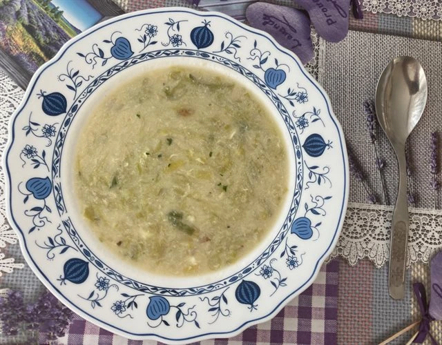 Pórková polévka s vejcem v misce vedle lžíče.