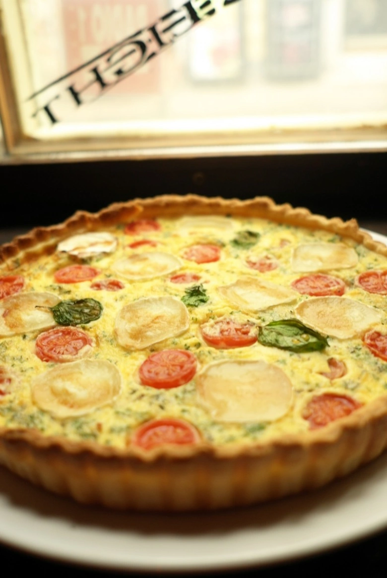 Hotová quiche s rajčaty a bramborami na bílém talíři.