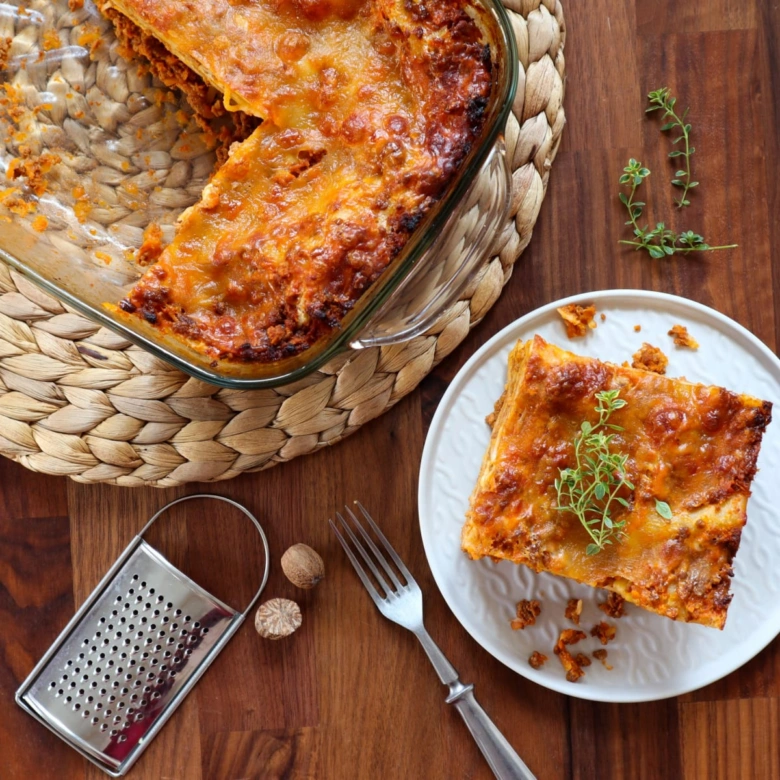 Kousek pečené lasagne s mletým masem na bílém talíři.