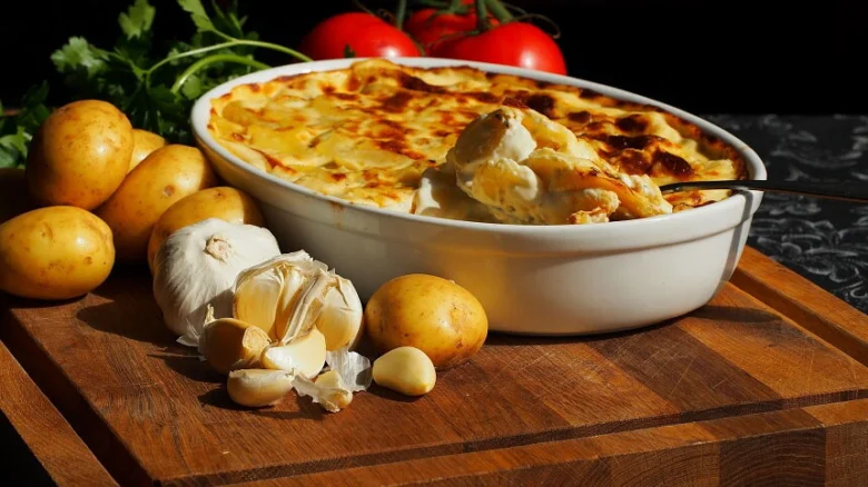 Gratinované brambory v bílé misce s česnekem a rajčaty.
