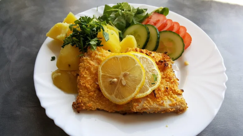 Opečené rybí filet s citronem, bramborami a zeleninou na talíři.