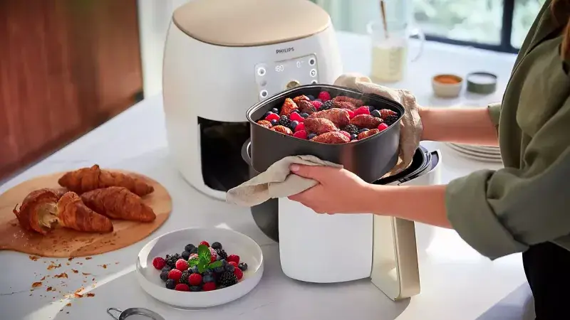 Osoba vyndává pečené ovoce z horkovzdušné fritézy vedle rohlíků.