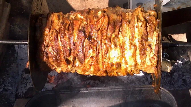 Obrázek ukazuje vařící se maso na točícím grilu pro gyros.