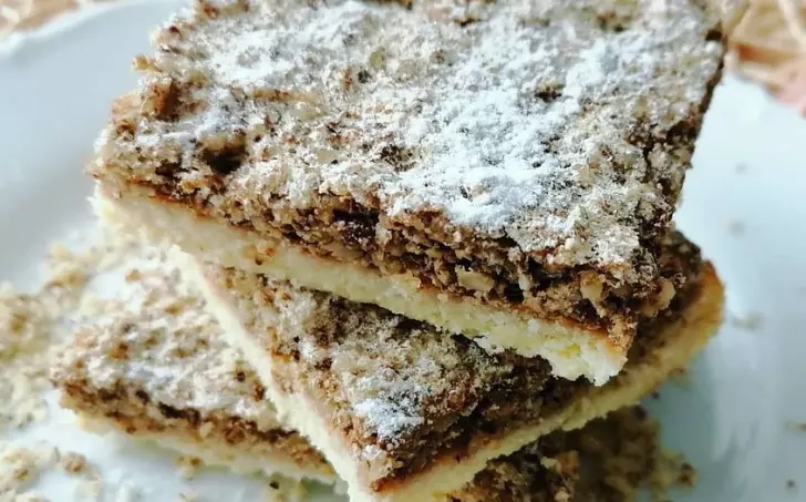 Skládané ořechové řezy posypané moučkovým cukrem na talíři.