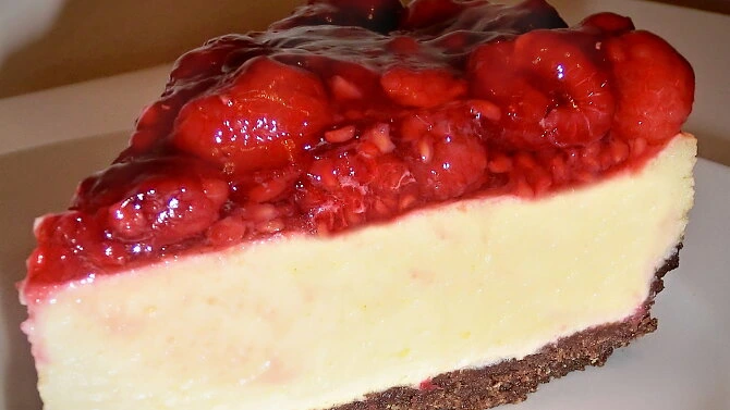 Kousek malinového cheesecaku s ovocnou omáčkou na bílém talíři.
