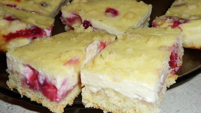 Čtyři čtvercové řezy s tvarohem a jahodovým náplní na tmavém talíři.
