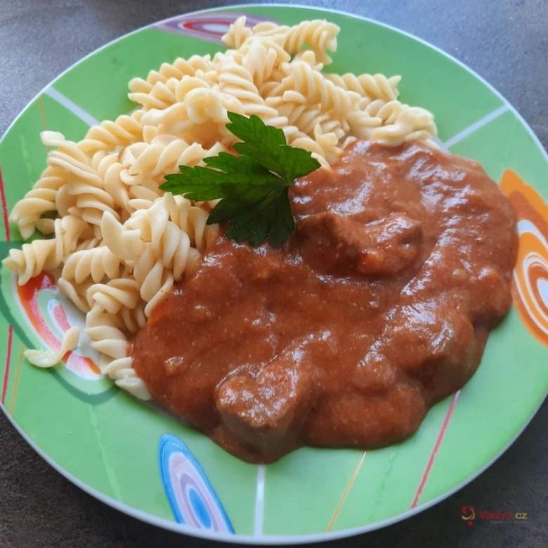 Pohár guláše s těstovinami na zeleném talíři.