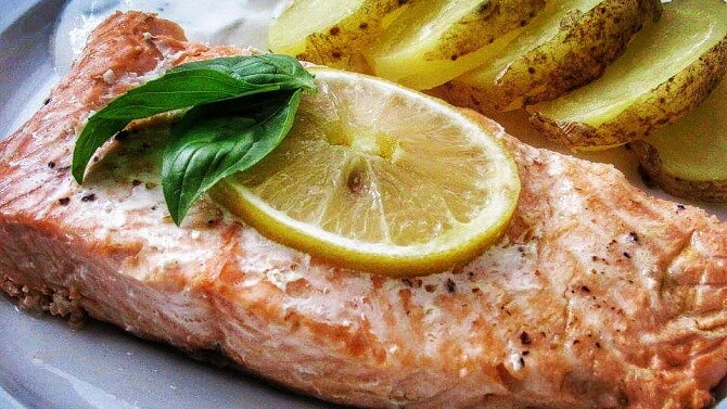 Upečený losos s citronem, bazalkou a pečenými bramborami na talíři.