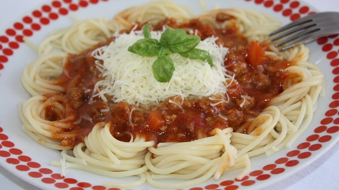 Spaghetti s boloňskou omáčkou, sýrem a bazalkou na talíři.