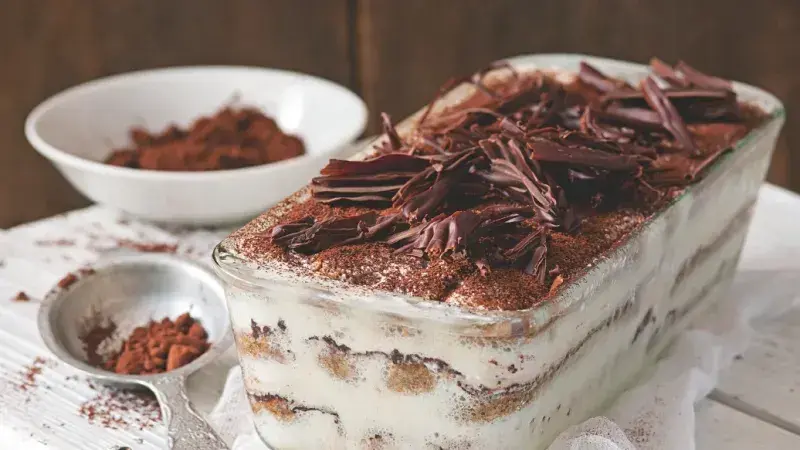 Tiramisu s čokoládovými lupínky a kakaem v skleněné misce.