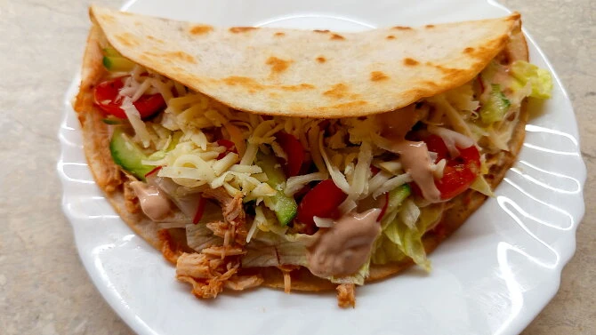 Taco s trhaným kuřecím masem na bílém talíři.