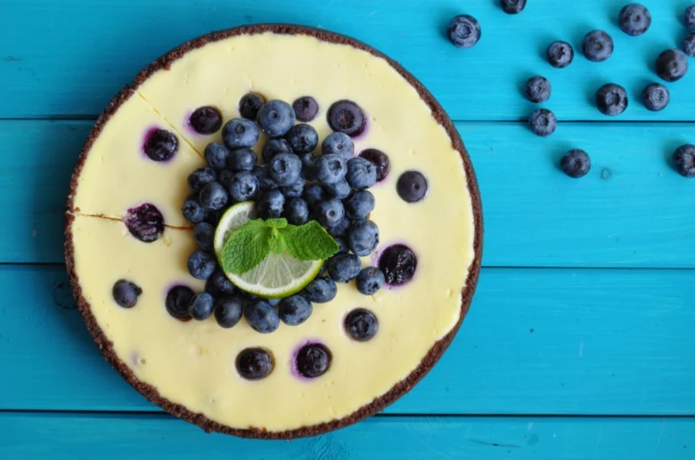 celý borůvkový cheesecake s limetkou a mátou na modrém dřevěném povrchu