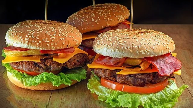 Tři domácí hovězí burgery s listovou zeleninou, rajčaty a sýrem.