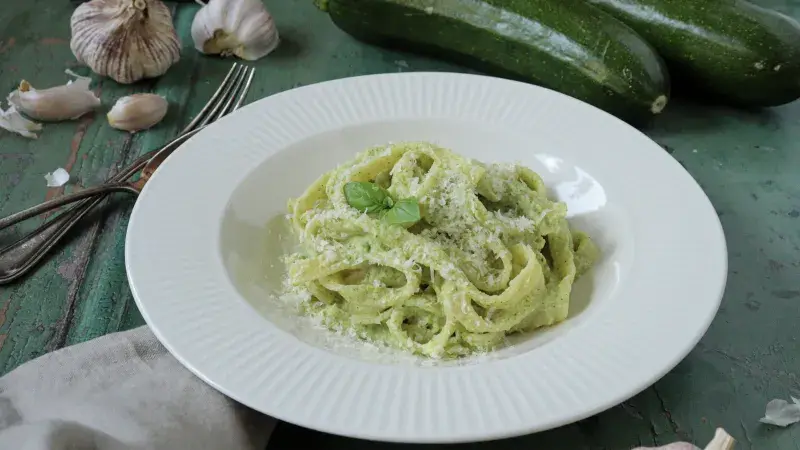 Pasta s cuketovou omáčkou posypaná syrem na bílém talíři.