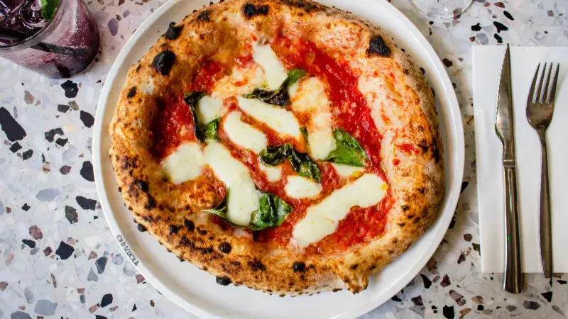 Neapolská piza s rajčatovou omáčkou, mozzarellou a bazalkou na talíři.