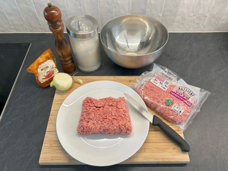 Surové hovězí maso s cibulí a kořením pro domácí burgery.