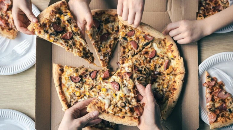 Lidé si rozdávají kousky domácí pizzy s uzeninou a zeleninou.