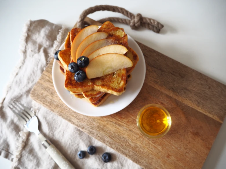 Zlatý francouzský toast s jablky a borůvkami na dřevěné desce.