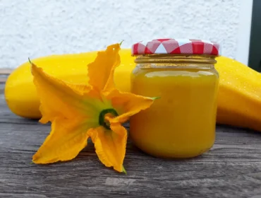 Sklenice cuketové omáčky s květem uzelky na dřevěném povrchu.