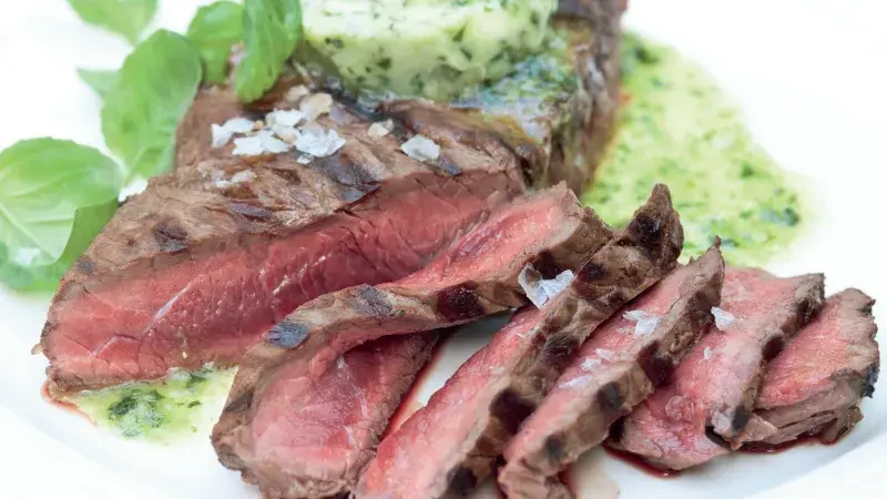 Opečený steak s bylinkovou omáčkou na bílém talíři.