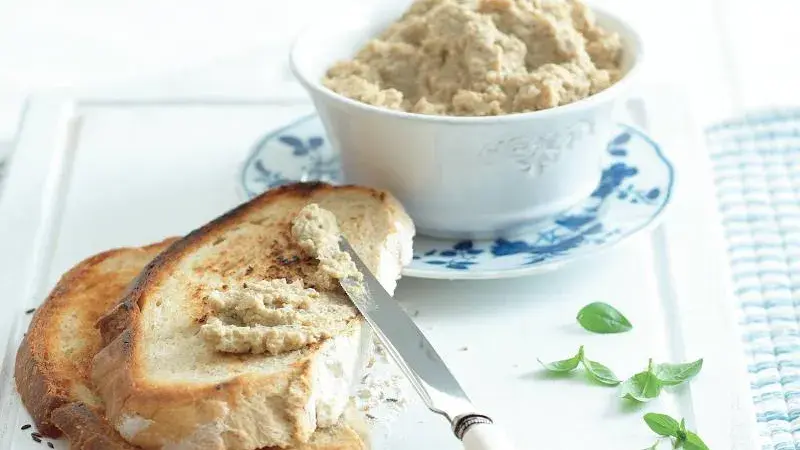 Mísa s hummusem na kouscích toastu rozmazaná nožem.