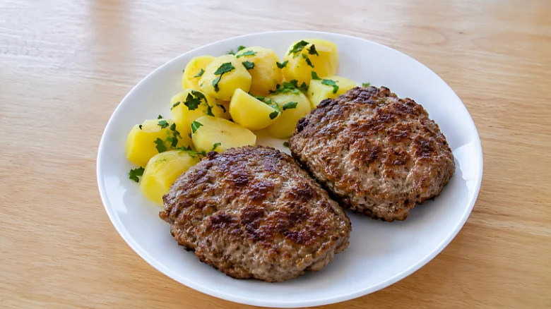 Dva smažené biftečky z mletého masa s bramborami na talíři.