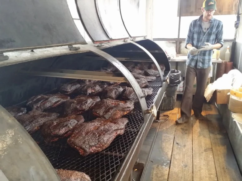 Muž připravuje trhané vepřové maso na velkém grilu.