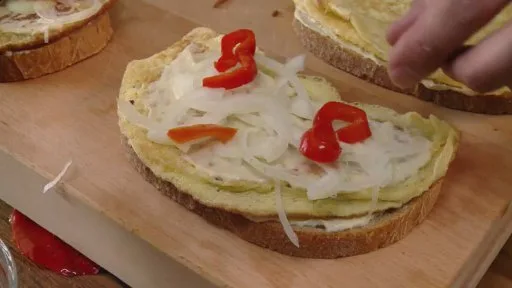 Kousek smaženky s cibulí, paprikou na dřevěném prkně.