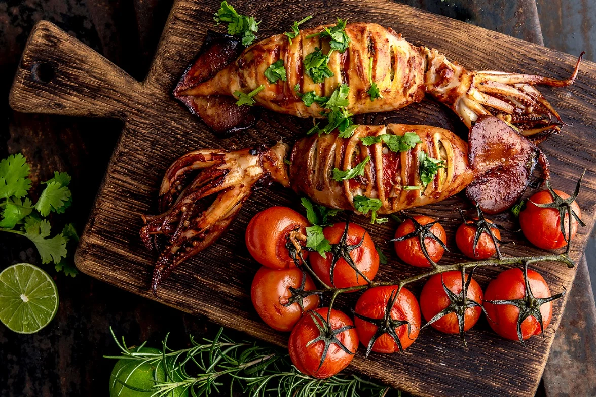 Grilovaný chobotnice s rajčaty a bylinkami na dřevěném prknu.
