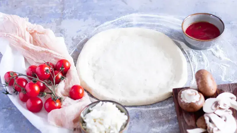 Nepekynuté těsto na pizzu s čerstvými ingrediencemi jako rajčata a houby.