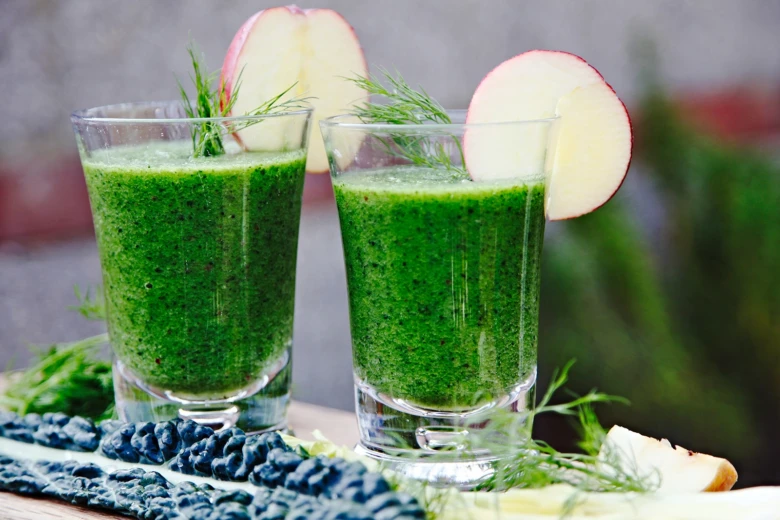 Dva sklenice zeleného smoothie s jablkem a koprem na dřevěném podkladu.