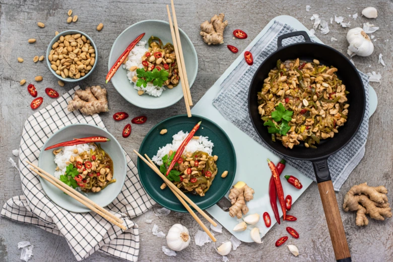 Kung pao vepřové s rýží, oříšky a kořením na dřevěném povrchu.