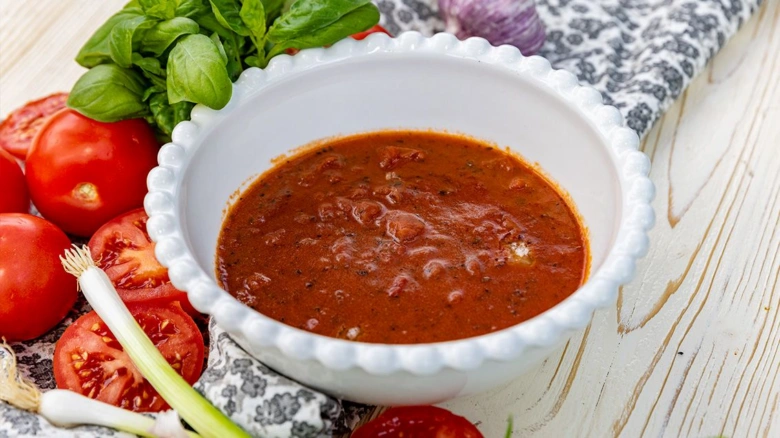Bílá miska s italskou rajčatovou omáčkou obklopená čerstvými ingrediencemi.