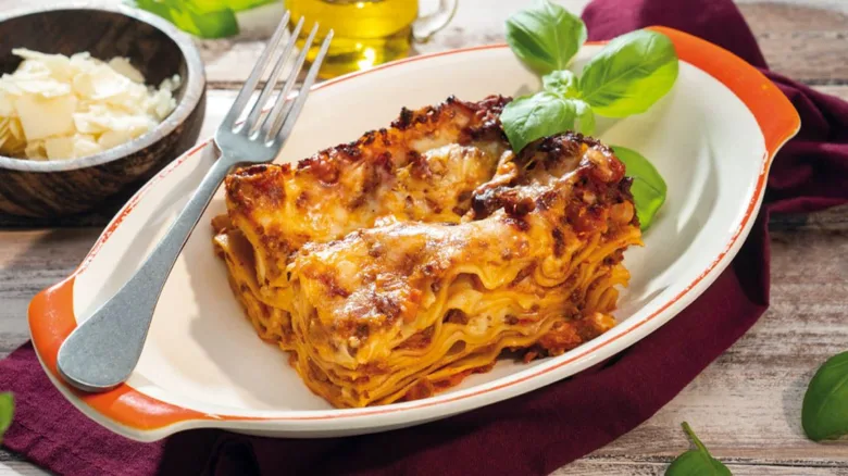 Kousek italské boloňské lasagni s bazalkou na talíři.