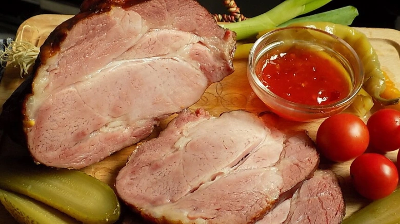 Uzená krkovice nakrájená na plátky s okurkami a rajčaty.