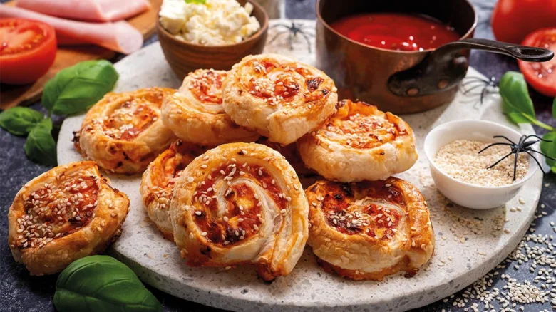 Zlatohnědé šneky z listového těsta s pizzou a sezamem na talíři.