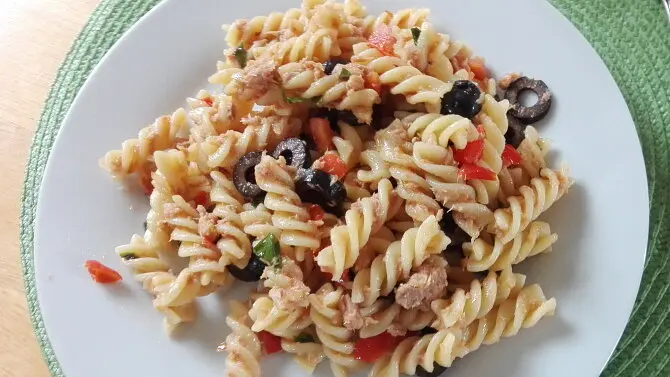 Pasta s tuňákem, okurkami, rajčaty a černými olivami na talíři.