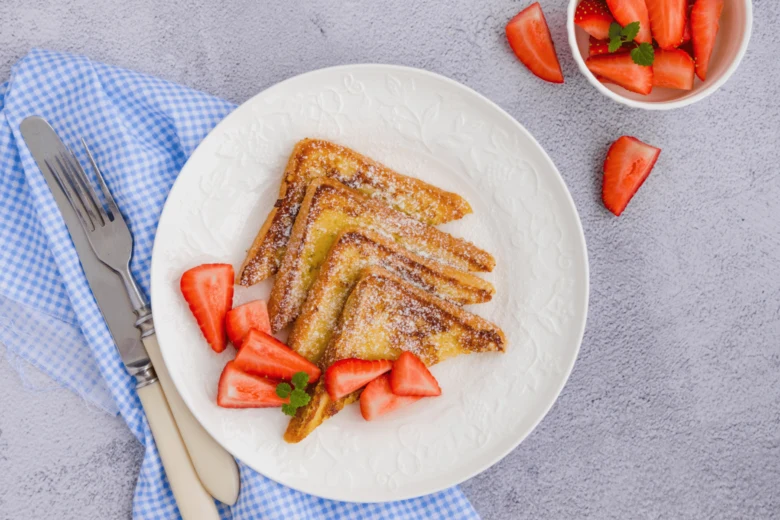 Zlatohnědý francouzský toast s cukrem a čerstvými jahodami.