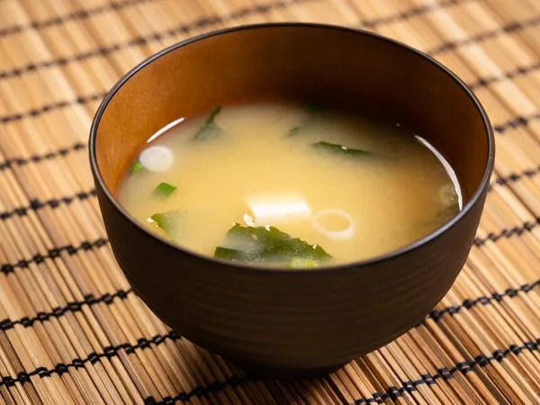 Miso polévka v tmavé mísce s tofu a řasami na bambusové podložce.