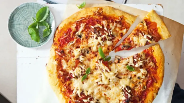 Domácí pizza s rajčatovou omáčkou, sýrem a čerstvým bazalkovým listem.