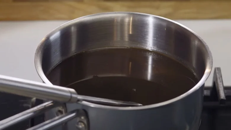 Nerezový hrnec s vařící omáčkou demi glace na plotně.