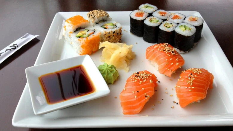 Bílá deska s různými druhy sushi, ryby a omáčkou.