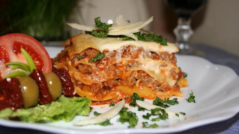 Kousek italské boloňské lasagne s mletým masem na bílém talíři.
