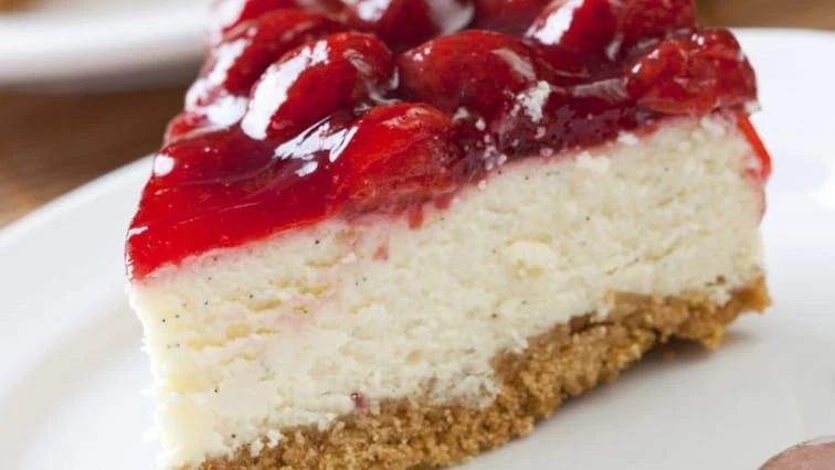Kousek jahodového cheesecaku s ovocnou polevou na bílém talíři.