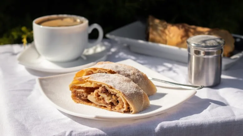 Kousek jablečného koláče s moučkou na bílém talíři.