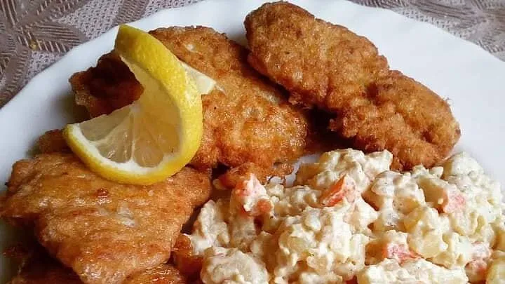 Savojský řízek s bramborovým salátem a citronem na talíři.