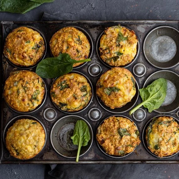 Zlatohnědé špenátové muffiny v plechu s čerstvými listy.